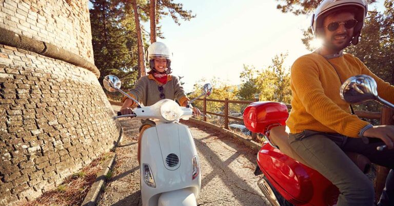 Bildet viser to personer på Vespa, ned en smal fjellvei.