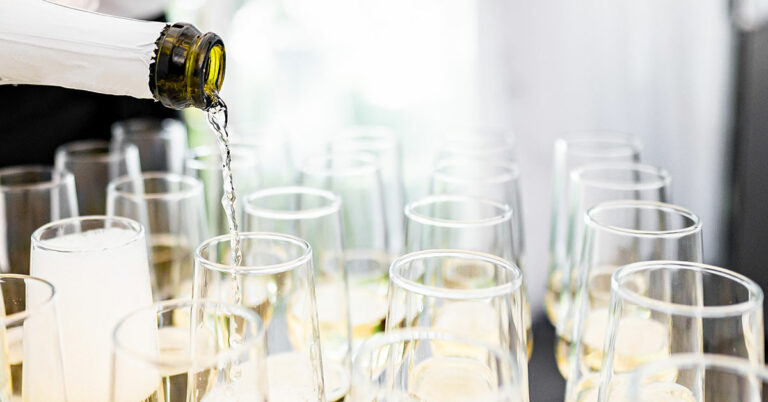 Bildet viser en flaske med Prosecco som helles oppi mange champagneglass.