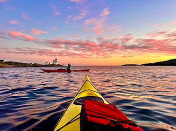 Bildet viser kajakkpadler i solnedgang foran Lyngør Fyr.