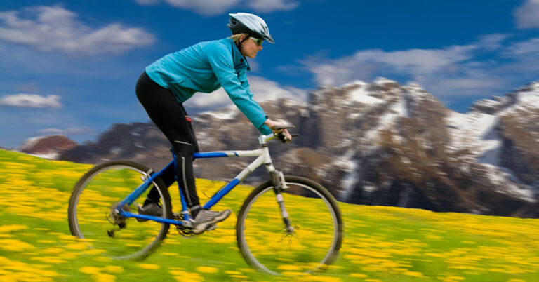 Jente på terrengsykkel (MTB) i blomstereng med fjell i bakgrunnen